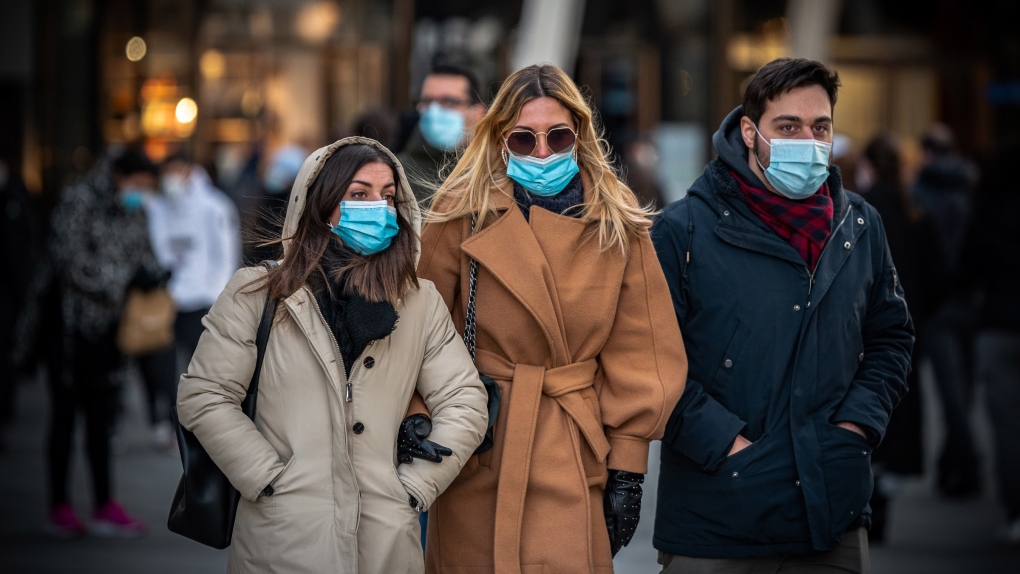 People wearing masks and dressed for cold weather walk arm in arm. (Photo by Matteo Jorjoson on Unsplash)