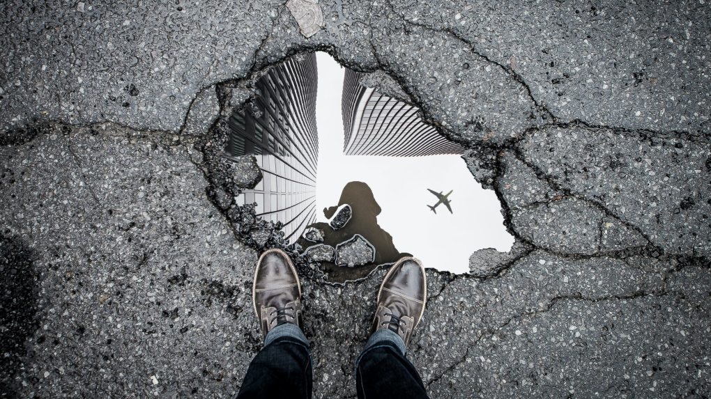 A person stands over a pothole in Ottawa, Ont. (Photo by Marc-Olivier Jodoin on Unsplash)

