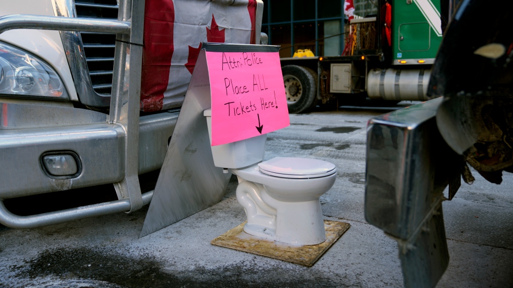 A sign points to a toilet, mocking police efforts to ticket protesters on the 18th day of a protest against COVID-19 measures that has grown into a broader anti-government protest, in Ottawa, on February 14, 2022. One year after the Freedom Convoy arrived in Ottawa, the city says a little more than half the cost of tickets handed out during the protests against COVID vaccine mandates have been paid. (Justin Tang/THE CANADIAN PRESS)